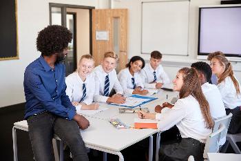 A teacher sitting on a desk talking to pupils