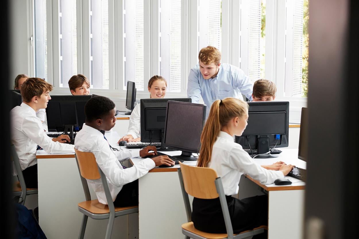 students engaged in computer class with teacher assisting