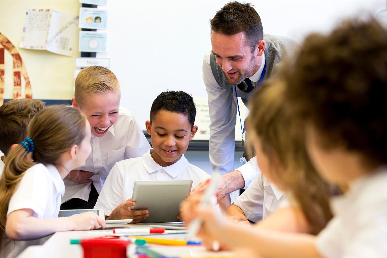 children engaging with a teacher while using a tablet in a classroom